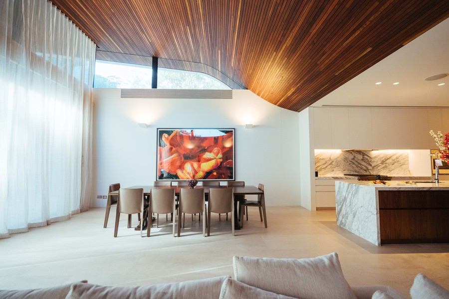 an open-concept dining room and kitchen area, with a lofty wooden ceiling and light filling the room.