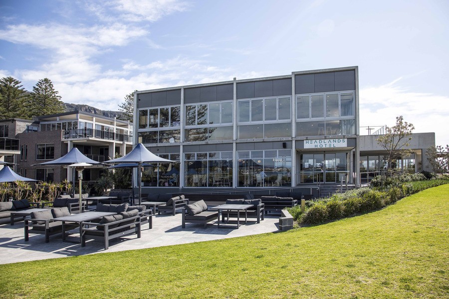 Exterior shot of the back patio at the Headlands Hotel featuring patio lounge chairs, tables and parasols with a view of lush green pasture in the foreground. 